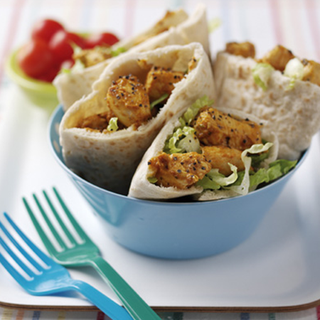 4 pitta bread pockets filled with marinated chicken pieces and shredded lettuce, served in a blue bowl with plastic forks on the side.