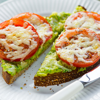 Sliced tomatoes on mashed avocados, covered in melted cheese and served on wholemeal toast.
